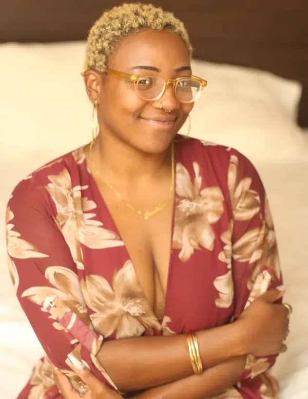 Close-up of Peach Fuzz in round glasses and a red floral dress, arms folded