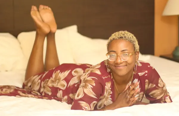 Peach Fuzz lying on her stomach on a bed in a red floral dress, feet kicked up